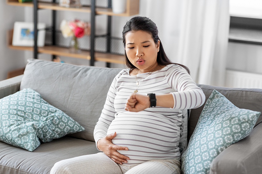 Pregnant woman touching her belly and checking her watch.